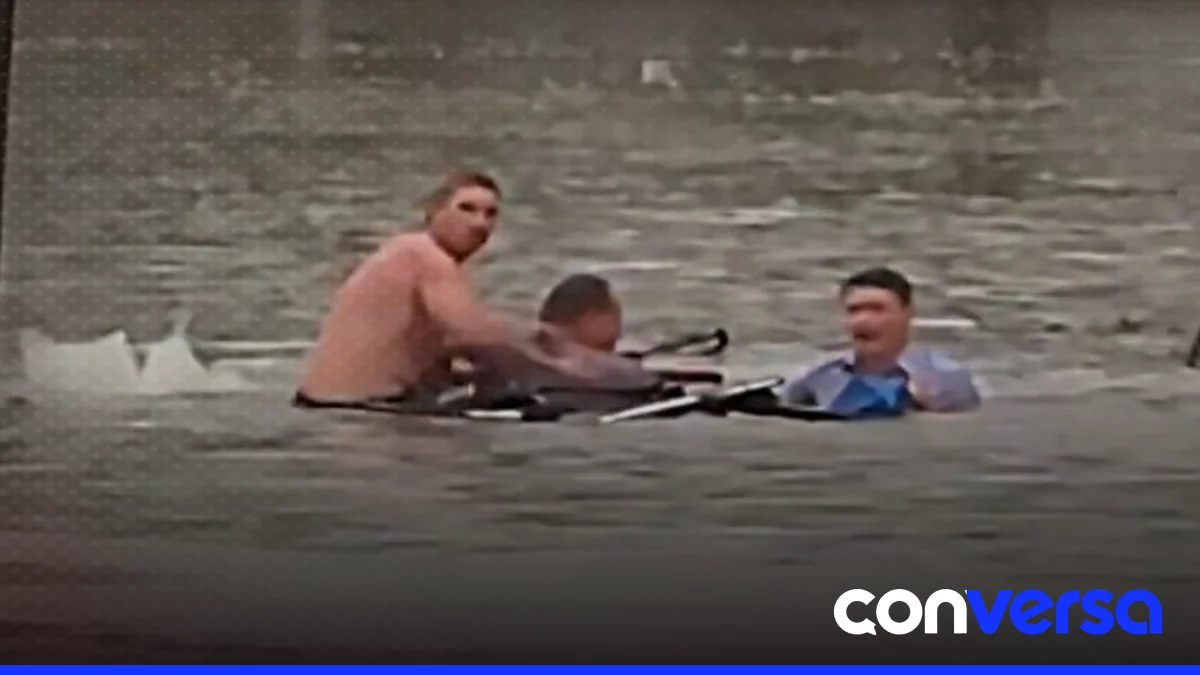 Imagen de un reportero y un transeúnte rescatando a un hombre atrapado en un vehículo durante una inundación.